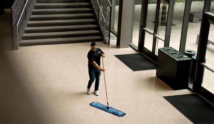 A professional using a dust mop to clean the tiled floor of a commercial space